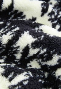 Pătură din fleece cu o suprafață moale și texturată; prezintă un model abstract alb-negru pe un fundal crem.