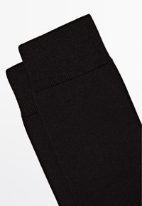 Sorte sokker lavet af et glat, strækbart materiale. Har en ribbet topkant, en sømløs krop og en ensfarvet overflade uden mønstre.