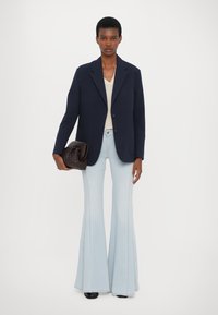 Navy blazer, cream v-neck top, light blue flared jeans, and a dark woven handbag. The outfit features clean lines and subtle textures.