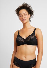 Black lace bra with scalloped edges, featuring a floral design. It has adjustable straps and a smooth band, paired with black lace-trimmed briefs.
