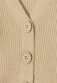 Beige stickad cardigan med ribbat mönster, V-halsdesign och tre stora, runda knappar i matchande färg.