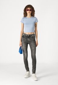 T-shirt courte bleu clair, jean skinny noir, baskets blanches, lunettes de soleil rouges et un petit sac à main bleu. Tissu lisse et design ajusté.