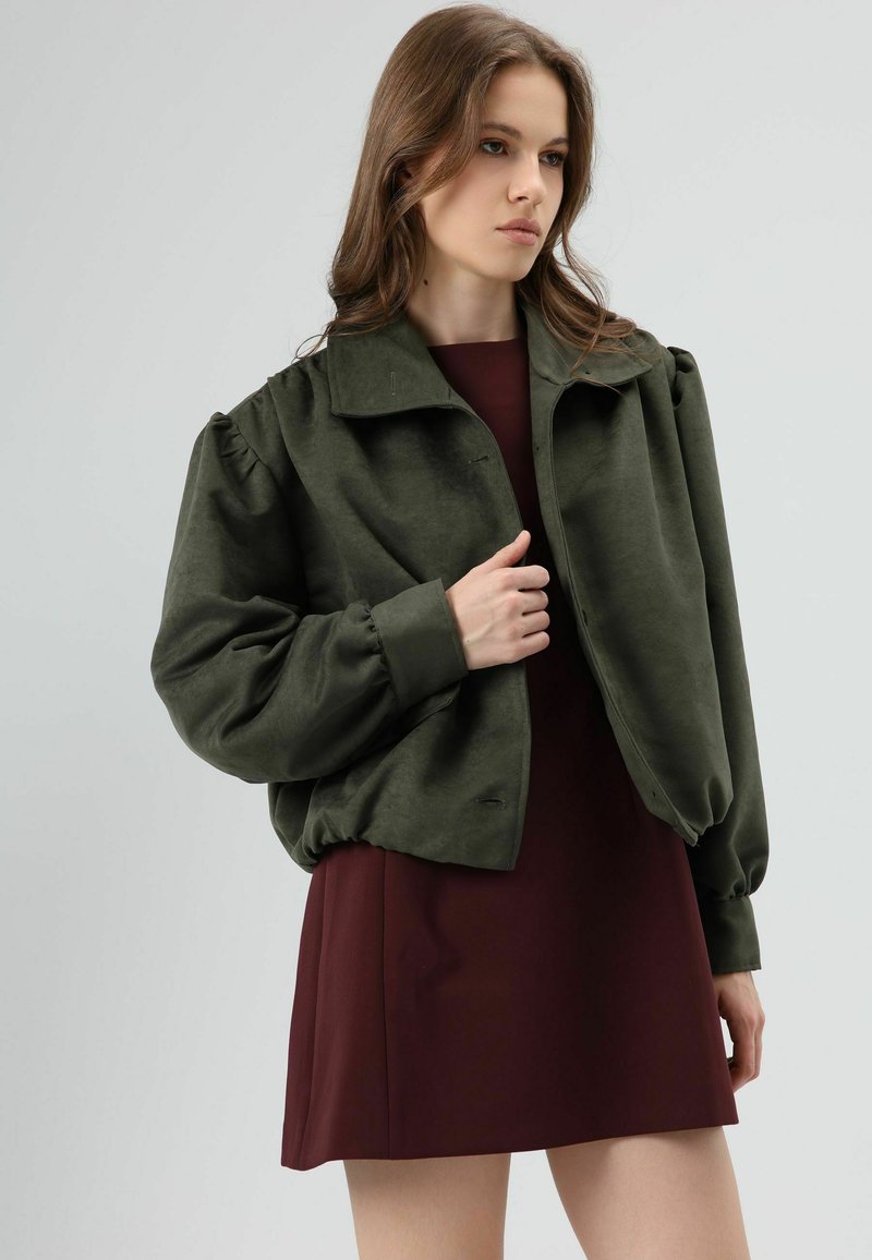 Veste courte vert olive à manches bouffantes, dotée d'un col classique et d'une texture douce, associée à une robe bordeaux.