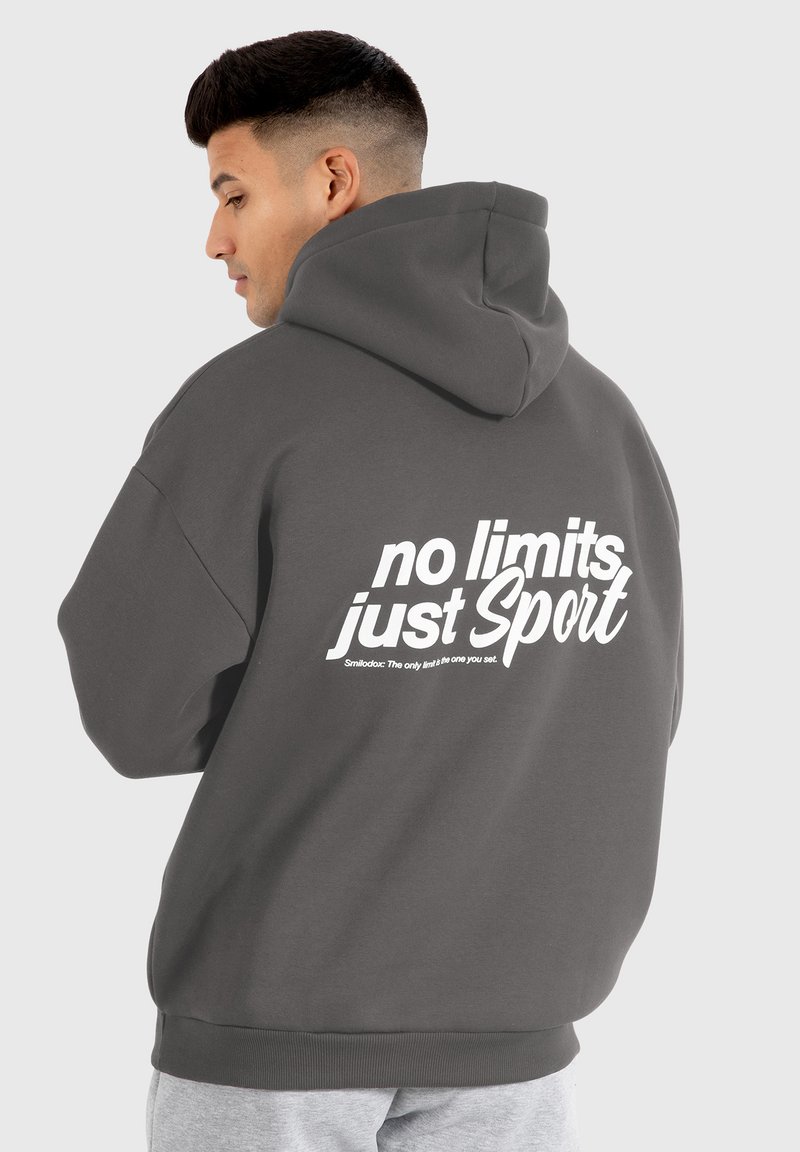 Felpa grigia con cappuccio, vestibilità comoda, con testo grafico bianco sul retro. Texture morbida, tasca a marsupio, polsini e orlo a coste.