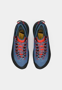 Blauwe klimshoeven met zwarte rubberen neus, rode veteren en een geïntegreerde tong. Beschikt over een getextureerde bovenkant en een duurzame, ondersteunende structuur.