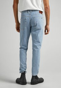 Ljusblå jeans med ränder och smal passform, med en läderpatch vid midjan, bakfickor och ankellängd, matchade med svarta stövlar.