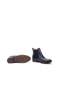 Bottes Chelsea en cuir noir avec des panneaux élastiques sur les côtés, un nez arrondi et un petit talon empilé. La semelle présente un motif texturé léger offrant une certaine adhérence.