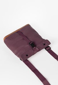 Lila synthetische Tasche mit einem Oberteil aus braunem Leder, verstellbaren Trägern und einer Vorderseite mit Schnalle. Sie verfügt über eine glatte Textur und gestickte Details.