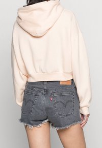Sweat à capuche court rose clair avec cordon de serrage, associé à un short en jean gris foncé usé avec un ourlet effiloché et des poches arrière.
