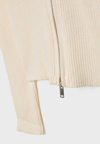 Kremowa sweterowa tkanina prążkowana z srebrnym zamkiem na dole. Posiada długie rękawy z prążkowanymi mankietami i skrócony krój.