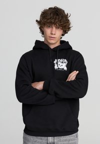 Felpa nera con tasca frontale, cappuccio regolabile con lacci e grafica che rappresenta un orso. Tessuto morbido e casual con polsini e orlo a coste.