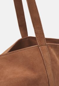 Brown suede tote bag with sturdy, flat handles and a clean, structured shape. Notable soft texture with precise stitching detail.