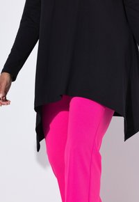 Haut noir à manches longues avec un ourlet arrondi associé à des pantalons ajustés rose vif. Le haut est en tissu lisse ; les pantalons sont extensibles et texturés.