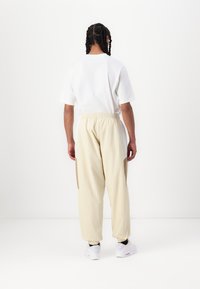 Camiseta branca de manga curta combinada com calças elásticas de cintura alta amarelas claras, com painéis laterais beges e sapatilhas brancas.