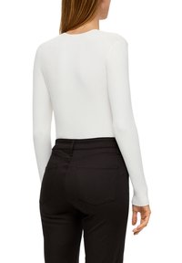 Witte lange mouwen ribtop met een ronde halslijn, gecombineerd met zwarte strakke pantalons met achterzakken. Glad textuur, getailleerde pasvorm.