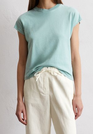 T-shirt bleu clair à manches courtes en matériau doux, associé à un pantalon à cordon de serrage de couleur crème avec des poches latérales.