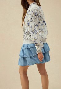 Sweat-shirt gris à motif floral avec poignets côtelés, associé à une jupe en denim bleu clair à volants. Les deux vêtements présentent un style décontracté.