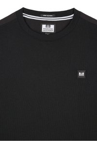 Sort T-shirt lavet af blødt stof med rund halsudskæring, der har et lille firkantet logo-patch på venstre bryst og stribede detaljer på kraven.