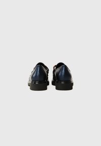 Navy leather shoes with a smooth texture, black rubber soles, and decorative cutouts; back view shows rounded heel and minimalistic design.