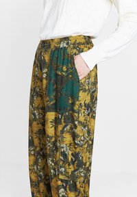 Bloemmotief, mosterdgele broek met een turkooizen accentzak, elastische tailleband en een relaxte pasvorm. Gemaakt van gestructureerde stof.