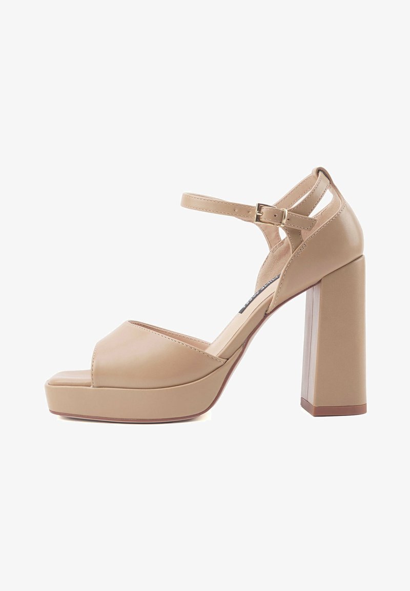 Sandali col tacco alto beige con tacco a blocco spesso, punta aperta e cinturino alla caviglia. Realizzati in materiale sintetico liscio con dettagli minimi.