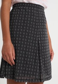 Gonna nera con motivo a rombi in bianco e grigio chiaro. Vita elastica e tessuto fluido con una leggera texture.