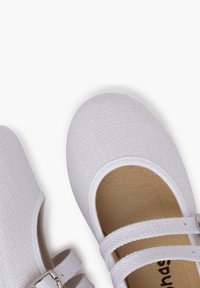 Baskets en toile blanches avec un bout rond, deux sangles élastiques, surface texturée et semelle intérieure brun clair. Design simple et plat, adapté pour un usage casual.