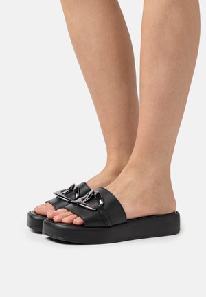 Black slide sandals featuring a smooth leather upper, two prominent decorative silver buckles, and a chunky black platform sole.