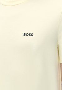 T-shirt jaune clair à manches courtes avec le mot « BOSS » imprimé en noir sur la poitrine.