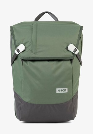 Zielony plecak z tkaniny z zwijanym zamknięciem, szarym spodem, regulowanymi paskami na ramiona oraz białymi plastikowymi elementami. Posiada przednią kieszeń.