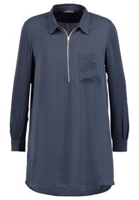 Chemise bleu marine à manches longues avec col, fermeture éclair et une poche poitrine. Tissu lisse avec une coupe légèrement ample et un ourlet arrondi.