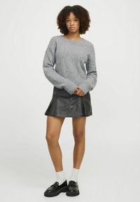 Maglione grigio lavorato a maglia con motivo a rombi, abbinato a una minigonna in pelle nera con pannelli e cuciture. Mocassini neri con tacco alto completano il look.