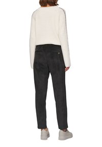 Zwarte corduroybroek met een rechte snit, voorzien van twee achterzakken. Gepaard met een off-white gebreide trui en lichte sneakers.
