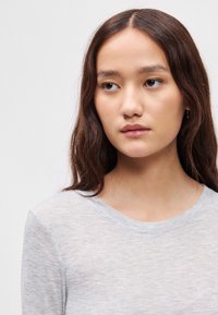 Svetlosivý dlhý rukáv top s okrúhlym výstrihom, vyrobený z mäkkej, textúrovanej tkaniny. Obsahuje priliehavý strih a minimálne švy.