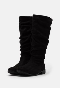 Bottes noires haute genou en daim doux avec un design relâché. Dotées d'une fermeture éclair sur le côté et d'un petit talon plat.