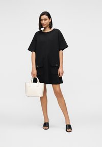 Μαύρο φόρεμα με κοντά μανίκια και δύο μπροστινές τσέπες, χρυσοί κουμπιά, σετ με λευκή δερμάτινη τσάντα και μαύρα σανδάλια slide.