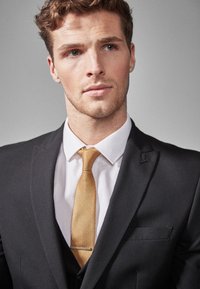 Black suit jacket with a white shirt underneath, complemented by a textured gold tie and a silver tie clip, featuring a classic design.