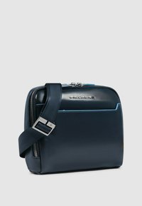 Dunkelblaues Leder-Crossbody-Tasche mit glatter Oberfläche, silberner Beschlägen und kontrastierender hellblauer Naht. Verstellbarer Gurt angebracht.