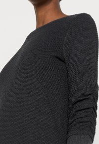 Black textured top with a ribbed pattern, boat neckline, and long sleeves. Fabric appears thick and slightly stretchy.