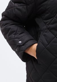 Μπουφάν σε μαύρο χρώμα με καπιτονέ υφή. Διαθέτει κουμπί με πατιλέτα στη μανσέτα και πλαϊνή τσέπη. Το υλικό φαίνεται ελαφρύ και μονωμένο.