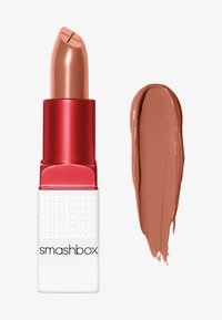 Rouge à lèvres nude avec une texture crémeuse dans un tube rouge et blanc. À côté, un échantillon de la même teinte sur une surface plane.