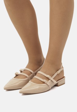 Bailarinas de charol beige con punta afilada, dos correas en el tobillo y hebillas doradas; pequeños tacones de bloque proporcionan estabilidad. Textura suave.