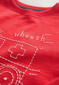 Red sweatshirt featuring white embroidered design with the word "whoosh" and a medical cross symbol. Smooth texture, crew neck style.