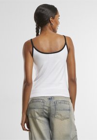 Biele tielko s čiernym lemovaním na výstrihu a ramienkach, v kombinácii s svetlomodrými voľnými džínsami s dvoma zadnými vreckami.