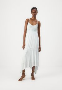 Gaiši zils maxi kleita ar regulējamiem spageti siksniņām, teksturētu augšdaļu un slāņotu volānu apakšu. Valkāta ar siksnām brūnām kurpēm.