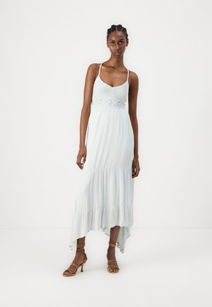 Abito maxi azzurro chiaro con spalline regolabili, corsetto testurizzato e orlo a strati con volant. Indossato con décolleté marroni con cinturini.