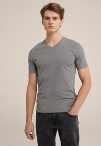 Tricou gri cu mânecă scurtă și decolteu în V, fabricat dintr-un material moale, având un design ajustat și o textură fină, asortat cu blugi închiși la culoare.