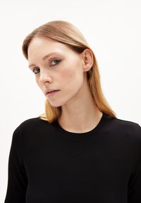 Schwarzes geripptes Langarmoberteil mit rundem Ausschnitt und weicher Textur, kombiniert mit glattem, hellbraunem Haar.