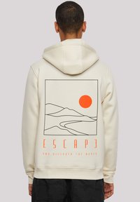 Sweatshirt crème avec un design graphique de montagnes et d'un soleil orange. Le texte en dessous dit "ÉVADER ET DÉCOUVRIR LE MONDE."