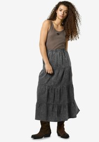 Pilkas sluoksniuotas maksi sijonas su elastinga juosta, derinamas su prigludusia rudąja marškinėlių palaidine. Modelis dėvi rudus kulkšninius batus. Tekstūruota medžiaga.